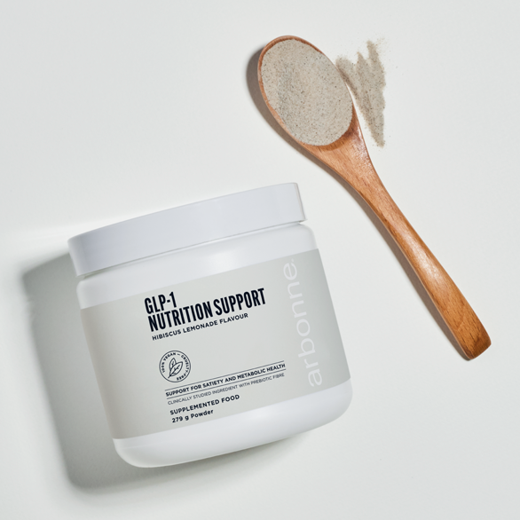 A tub of GLP 1 Nutrition Support hibiscus lemonade flavour with a wooden spoon of powder beside it